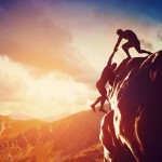 One person helping another person up a mountain