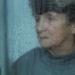 An older lady looking sad and starting out the window at rain drops