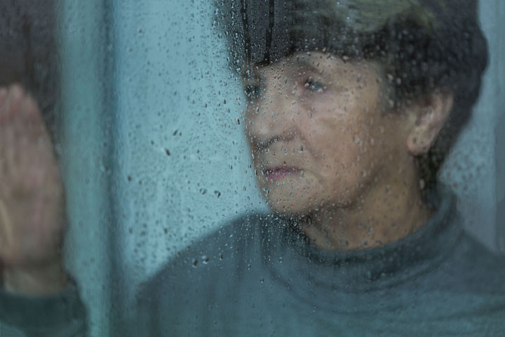 An older lady looking sad and starting out the window at rain drops
