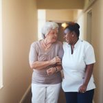 Happy female caregiver and senior woman walking together F