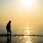old man walking in the sea during sunrise