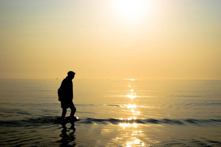 old man walking in the sea during sunrise