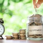 Hand putting Coins in glass jar with retro alarm clock , retirement