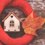 toy house is wrapped in a warm scarf with an autumn leaf. The concept is warm, cozy, loving, protecting the house.
