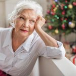 Charming sad old woman is sitting on sofa