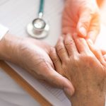 A healthcare worker holding the hand of an elderly patient.
