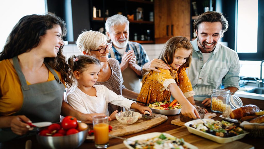 Family (grandparents, parents, and two children) at the island in the kitchen preparing for dinner