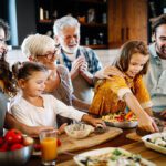 Family (grandparents, parents, and two children) at the island in the kitchen preparing for dinner