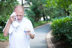 Older man out walking in the park. He is holding a water bottle in his left hand and toweling his face with his right hand. It appears to be a very hot day.