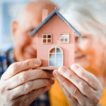 An older couple holding a model of a house.